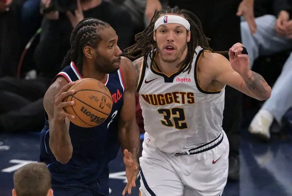 9 A player in a blue jersey dribbles a basketball while being closely guarded by an opponent in a white and gold uniform during a game.