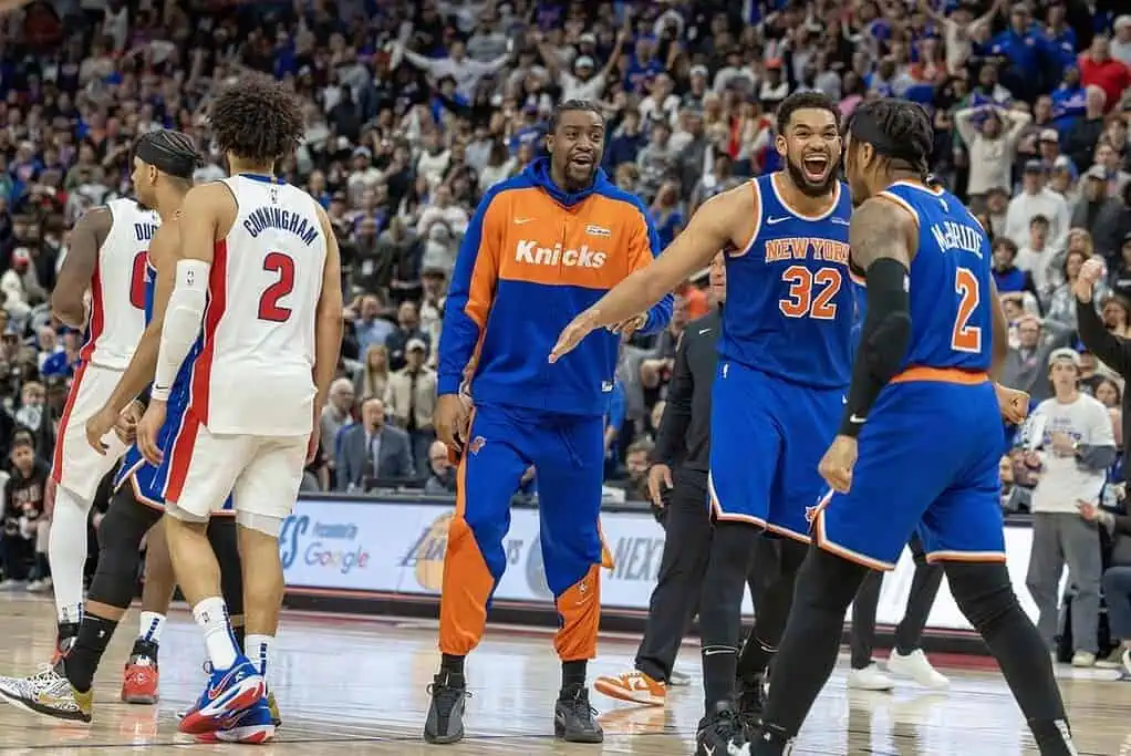 Players from the New York Knicks and Detroit Pistons interact on the court during an intense basketball game, surrounded by a cheering crowd.