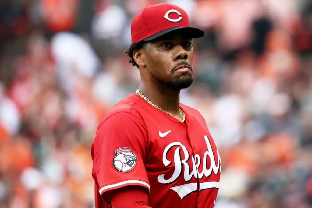 A baseball player in a bright red Cincinnati Reds jersey stands on the field, focused and ready for action amidst cheering fans.