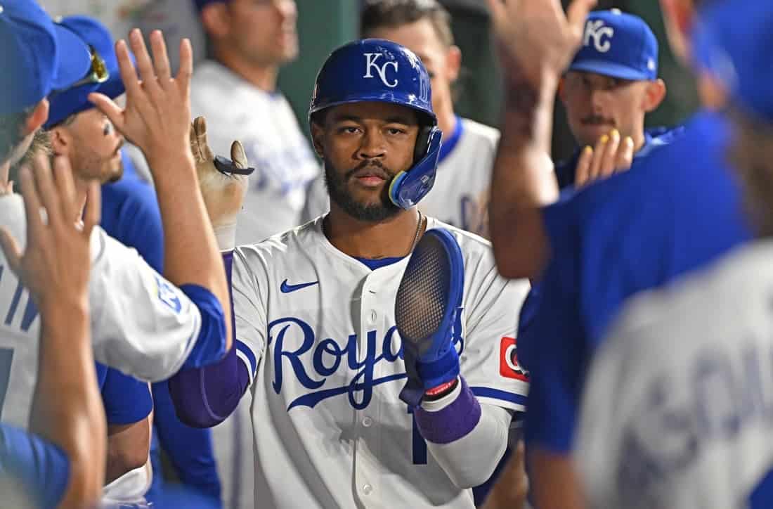 A baseball player in a Royals uniform celebrates with teammates, all raising their hands in a moment of camaraderie and excitement.