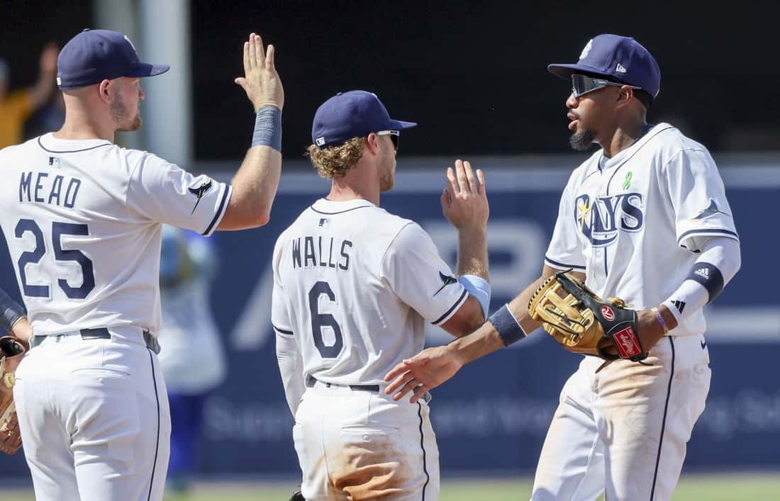 Three baseball players in Tampa Bay Rays uniforms engage in a high-five celebration on the field, demonstrating teamwork and camaraderie.