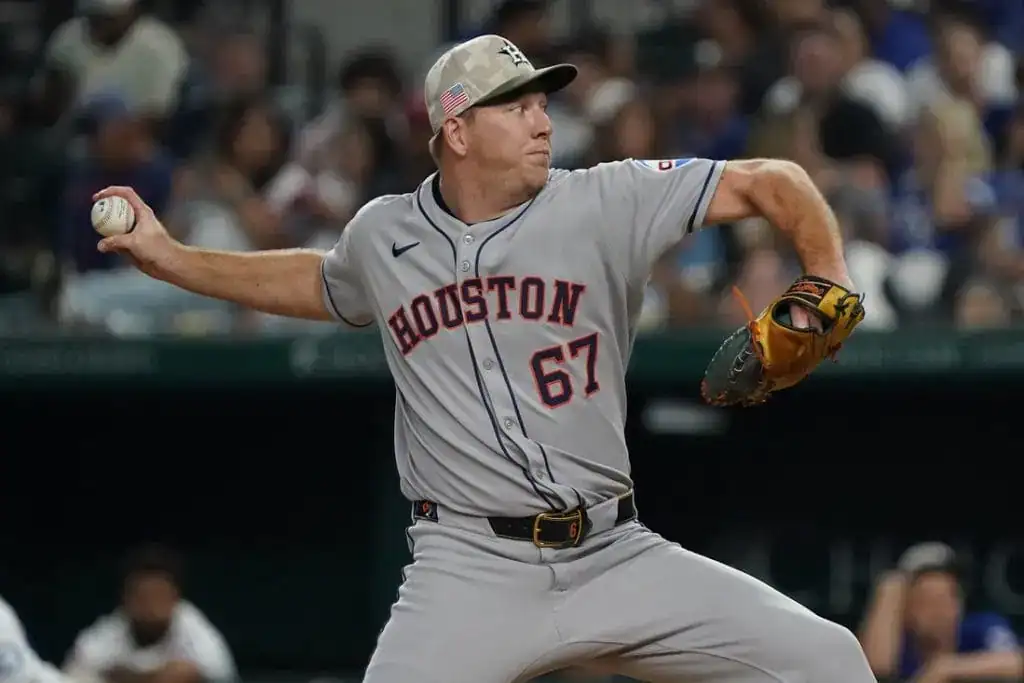 A baseball player in a gray Houston jersey prepares to pitch, gripping a baseball