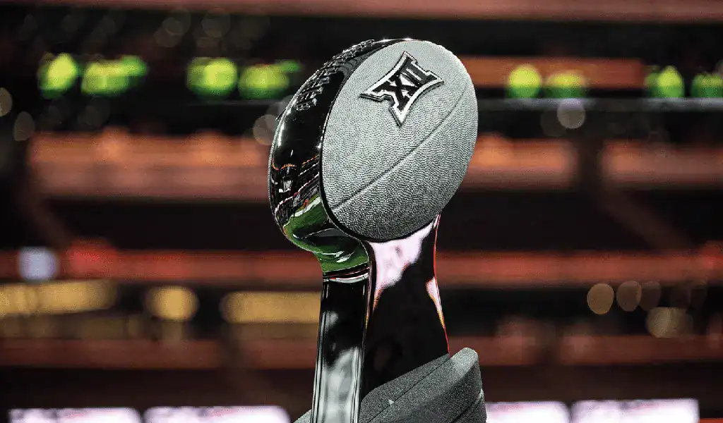 Trofeo con forma de balón de fútbol americano de la conferencia Big 12 sobre un fondo de estadio desenfocado