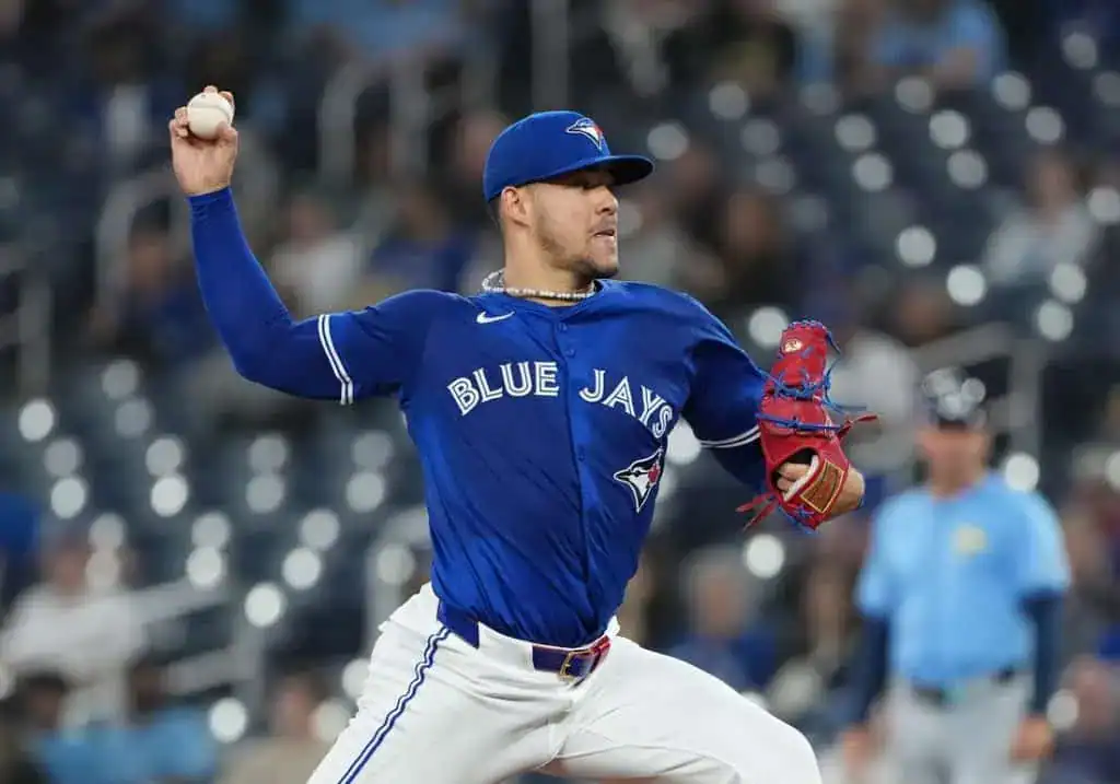 A Toronto Blue Jays pitcher prepares to throw a baseball during a night game, wearing a blue team jersey and red glove.