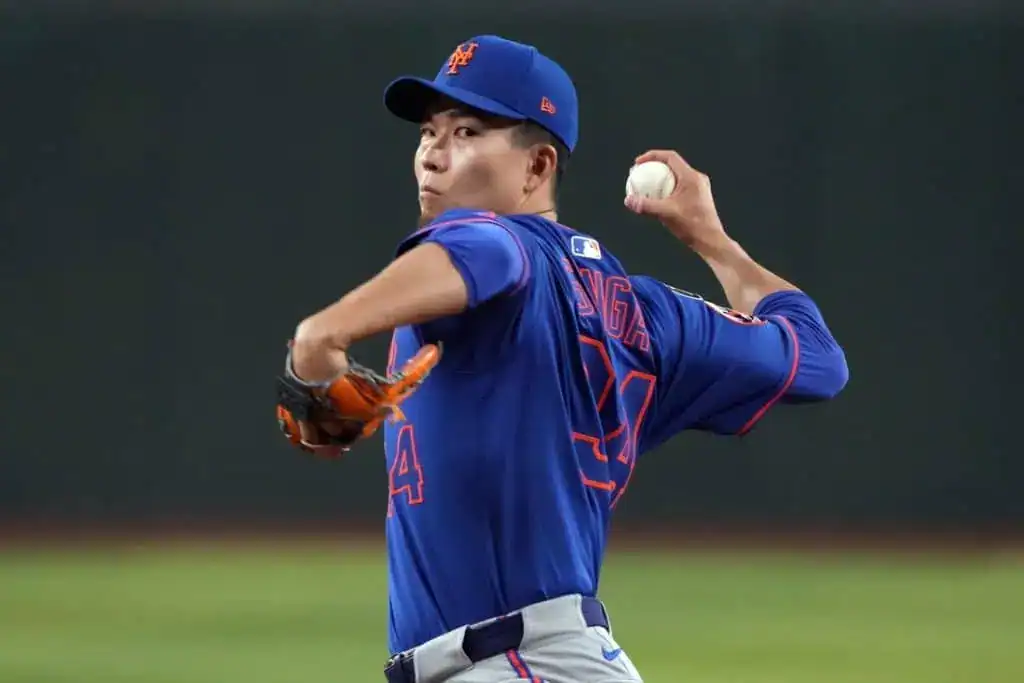 A baseball player in a blue Mets jersey prepares to pitch, holding a baseball with a focused stance on the field.