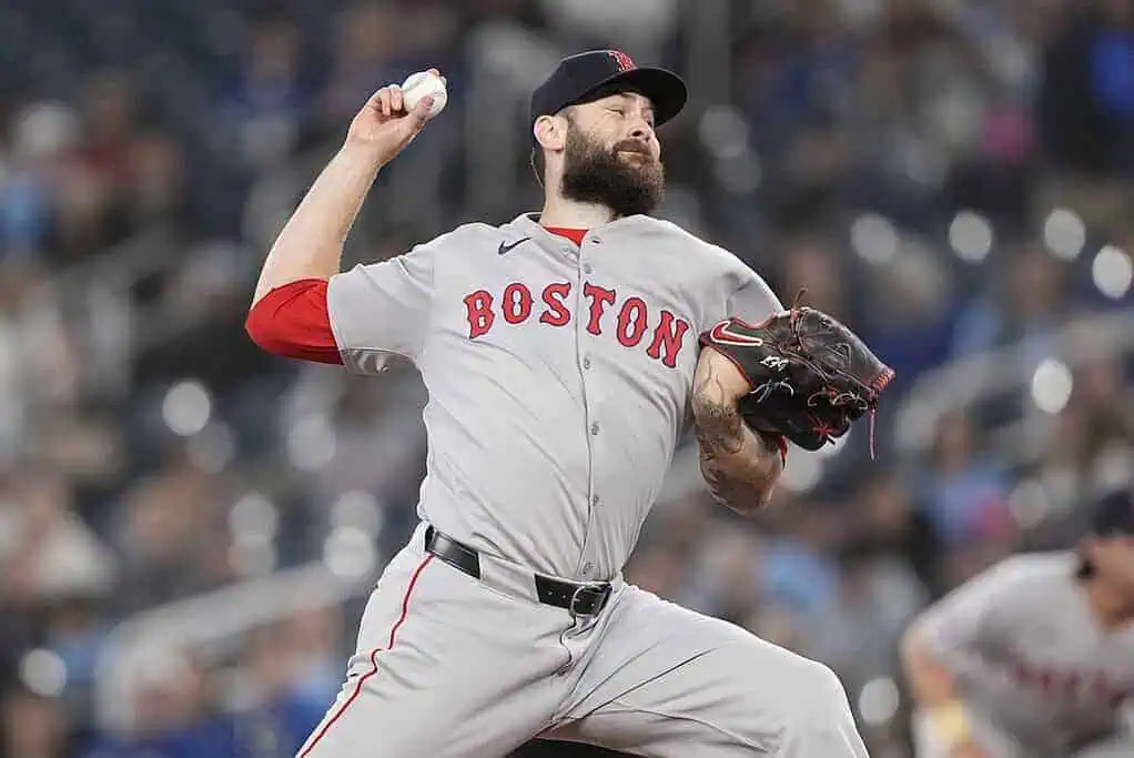 1 A Boston Red Sox pitcher in grey uniform winds up to throw a baseball during a night game