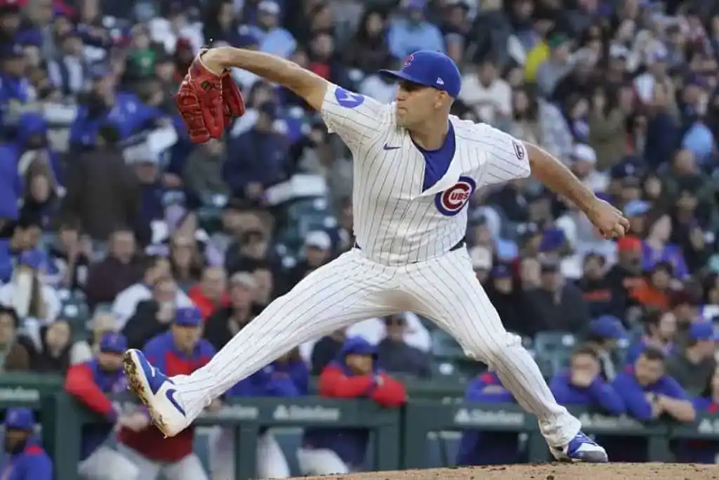 A Chicago Cubs pitcher in a home jersey winds up to throw a pitch.