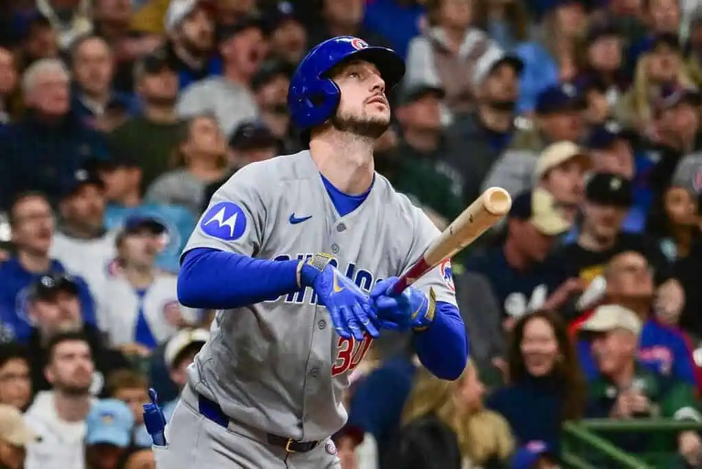 A Chicago Cubs player swings a baseball bat, surrounded by enthusiastic fans in a lively stadium atmosphere.