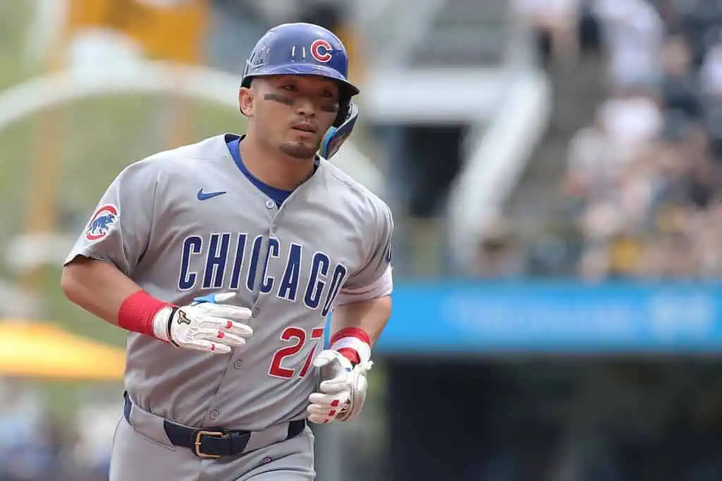A Chicago Cubs player runs the bases, wearing a gray jersey with "CHICAGO" and the number 27, on a sunny ballpark day.