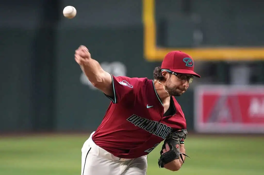 A baseball pitcher in a red Diamondbacks uniform throws a ball with intense focus, showcasing athleticism in a game setting.
