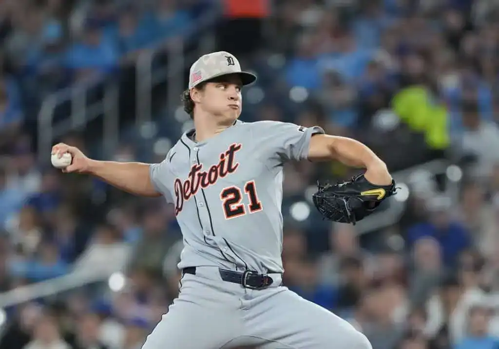 7 A baseball player in a uniform throws a ball on an outdoor baseball field, surrounded by stadium seating and baseball equipment.