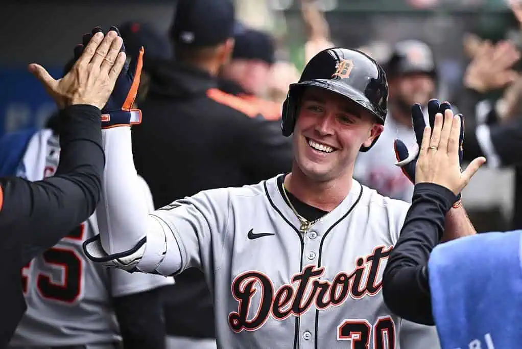 A baseball player in a Detroit Tigers jersey celebrates with teammates in the dugout, exchanging high-fives, showcasing team spirit.