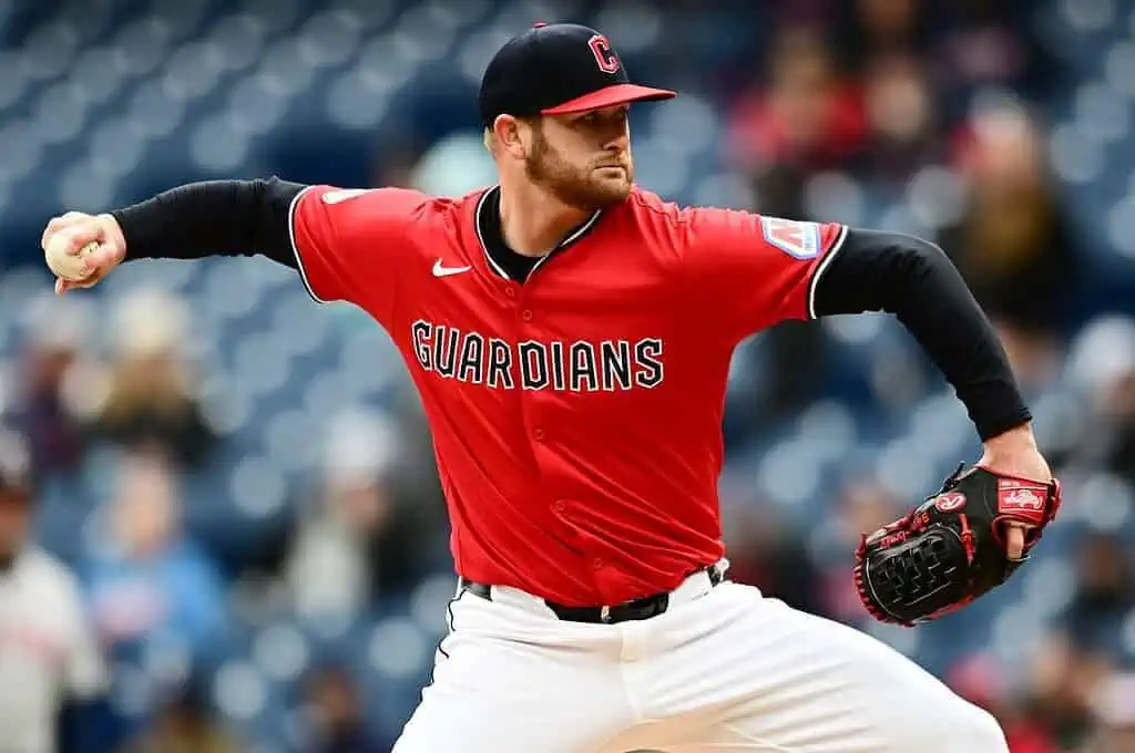 A pitcher in a red Guardians jersey winds up to throw a baseball on the field, showcasing a dynamic action pose.