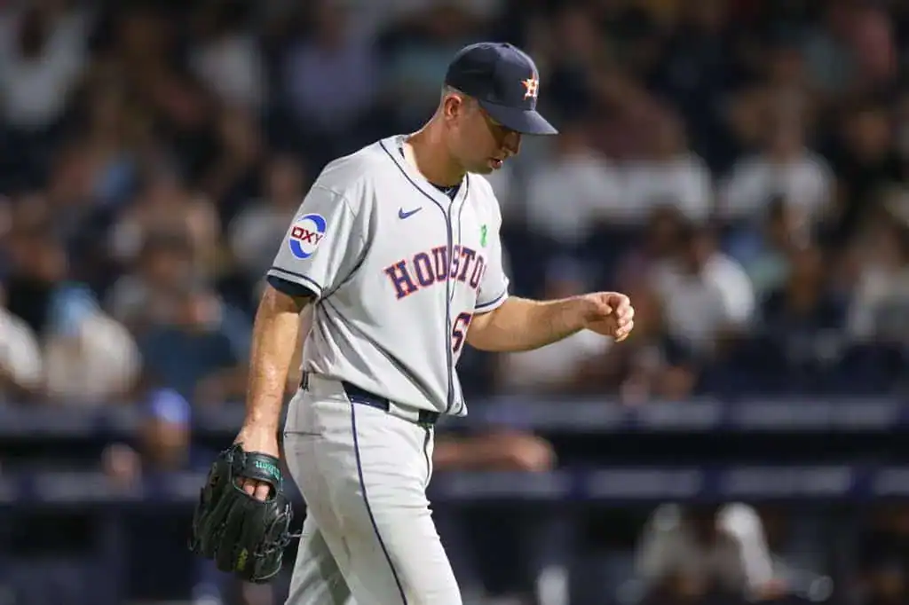 A baseball player in a Houston Astros uniform walks off the field, holding a glove, with fans blurred in the background.