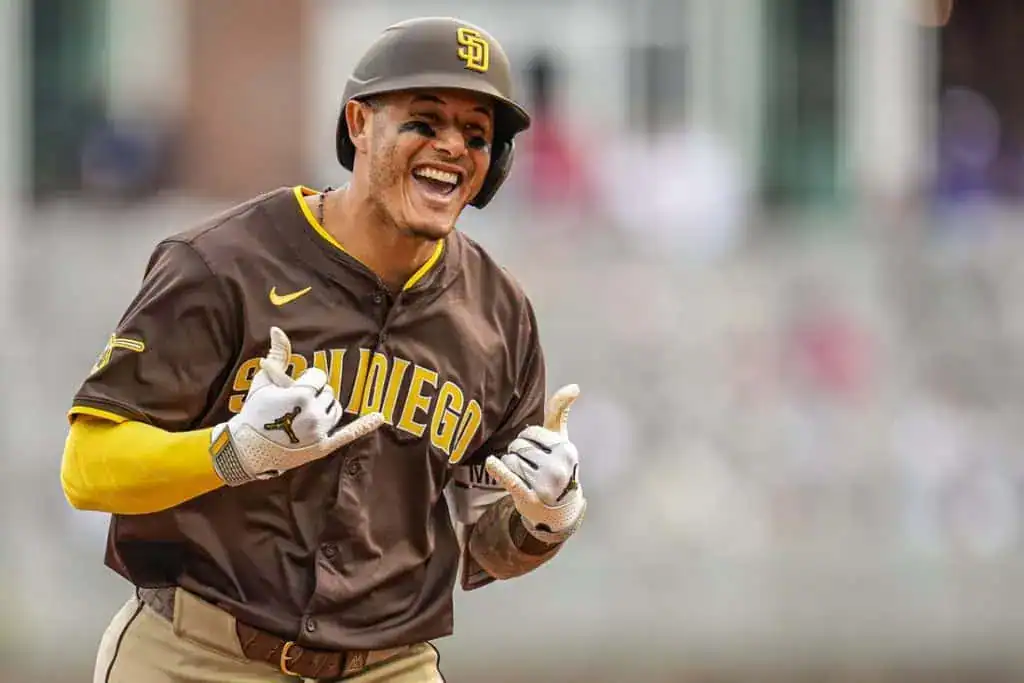 A baseball player in a brown San Diego jersey celebrates a play, making a hand gesture with a blurred stadium background.
