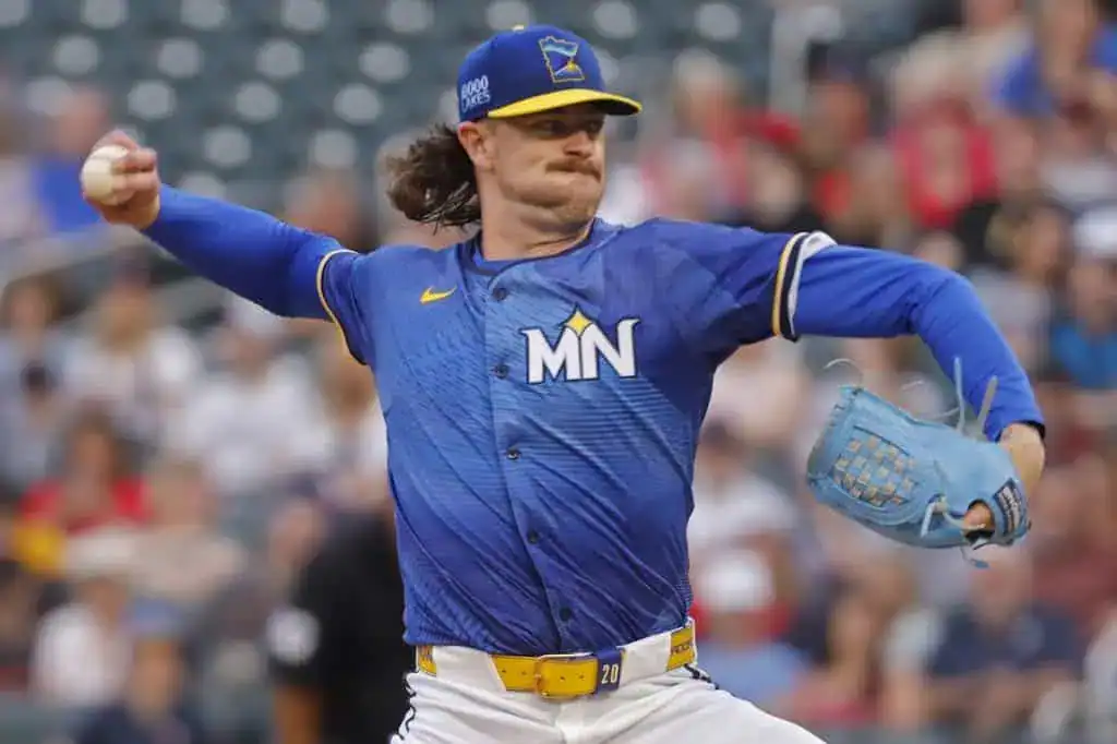 A baseball pitcher in a blue jersey delivers a pitch on the mound