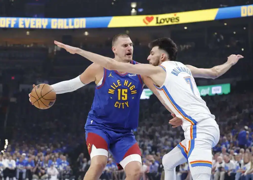 A basketball player in a blue "Mile High City" jersey faces an opponent in an Oklahoma City Thunder uniform, with intense defensive action.
