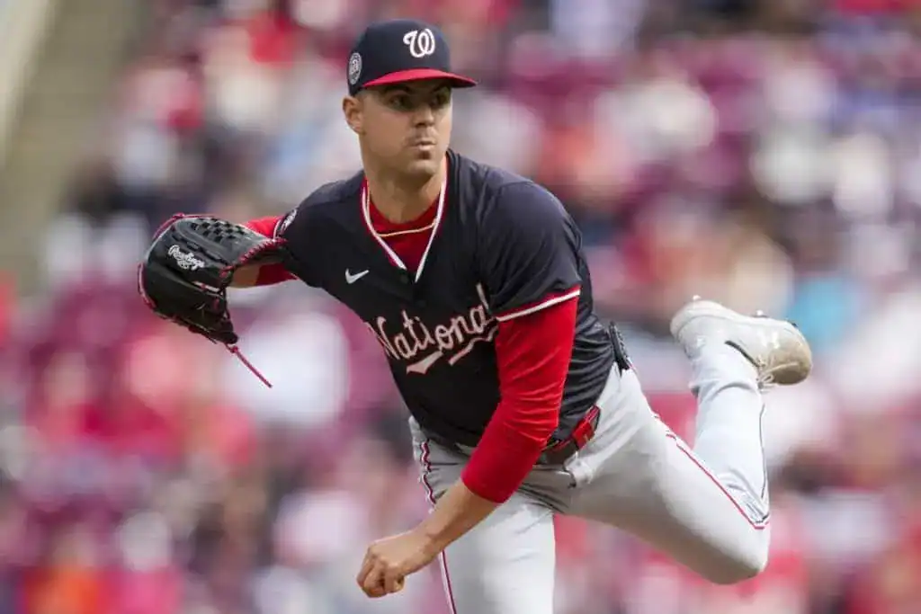 5 A pitcher in a navy and red baseball jersey, in mid-delivery, showcasing athleticism on a baseball field with a crowd in the background.