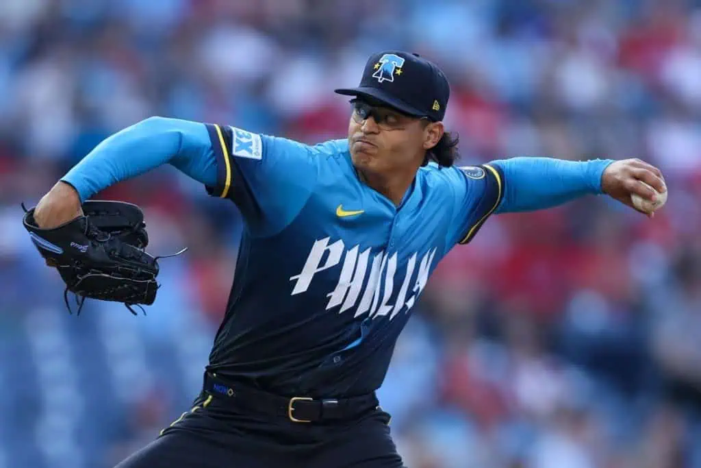 A baseball player in a blue and black jersey throws a pitch, showcasing athletic form on the field during a game.