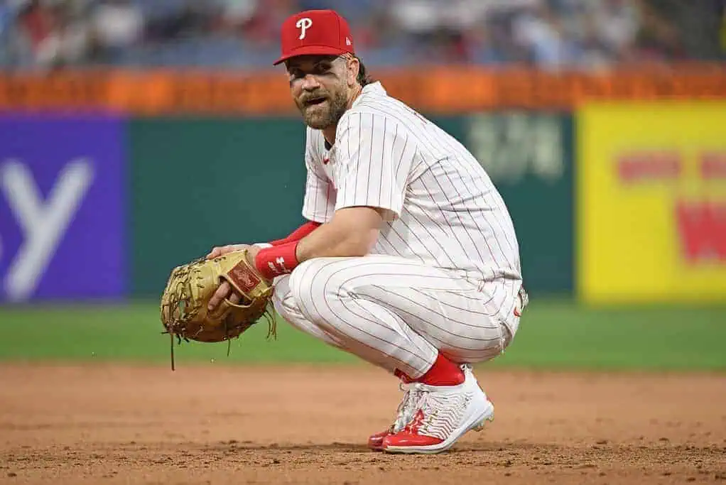 A baseball player in a white pinstripe uniform crouches on the field, wearing a red cap and cleats, ready for action.