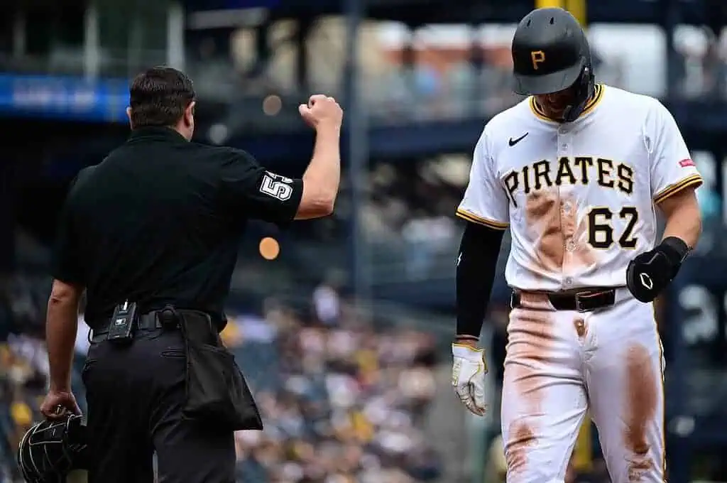 An umpire signals an out as a Pittsburgh Pirates player in a muddy uniform walks away, visibly disappointed during a game.