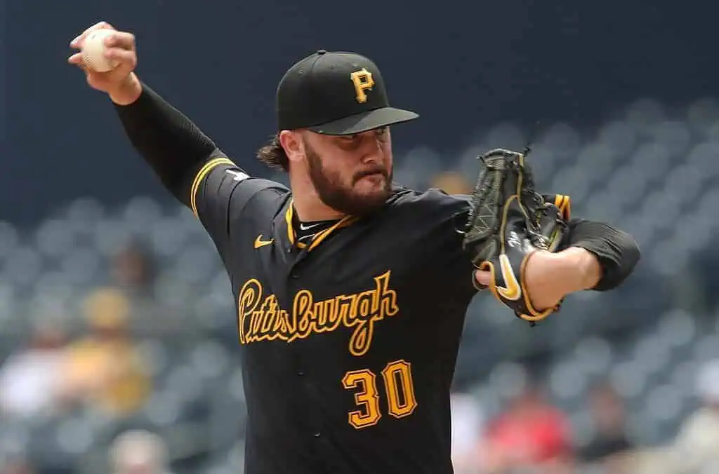 A baseball pitcher wearing a black Pittsburgh Pirates jersey prepares to throw a pitch, gripping the baseball in his right hand.