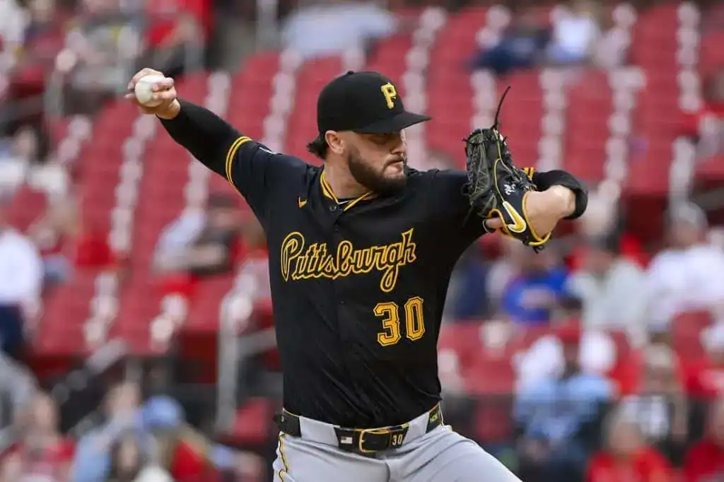 9 A pitcher in a black Pittsburgh Pirates jersey winds up to throw a baseball in a ballpark with empty red seating in the background.