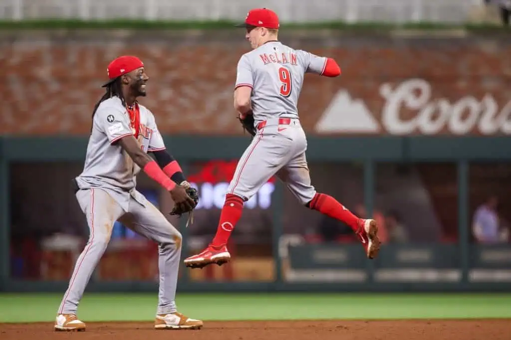 Two baseball players in gray uniforms, one in mid-leap to catch a ball, the other poised with a glove on the field.