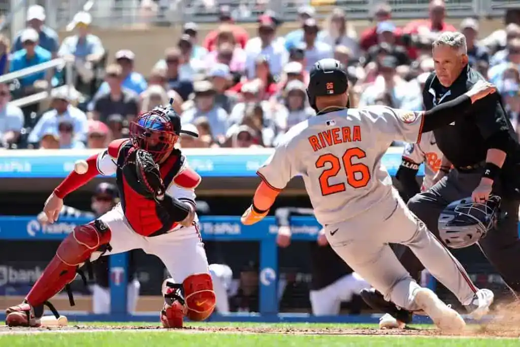 A baseball player, Rivera, slides towards home plate as a catcher prepares to receive a pitch during a game. The crowd watches intently.