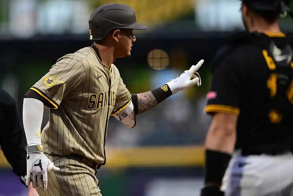 A baseball player in a tan striped uniform gestures emphatically towards an opposing player during a tense moment on the field.