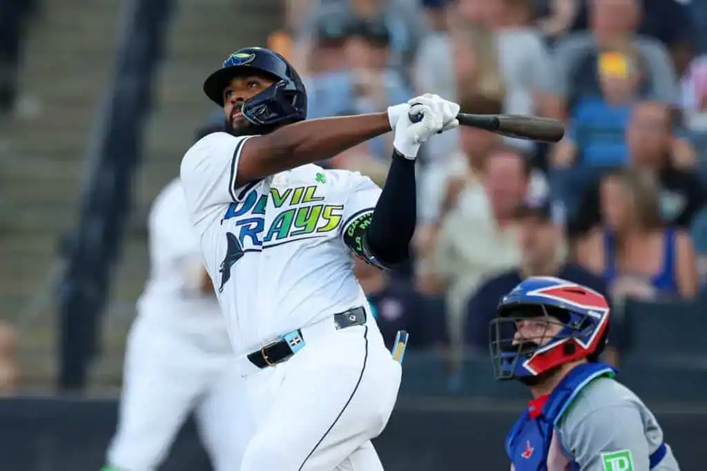 3 A baseball player in a blue and white jersey swings a bat during a game, with an audience visible in the background.