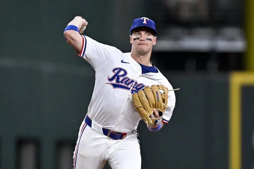 A Texas Rangers player in a white jersey and glove prepares to make a throw during a night baseball game.