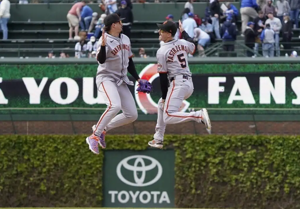 Two San Francisco Giants players celebrate a play by jumping in the air on the baseball field