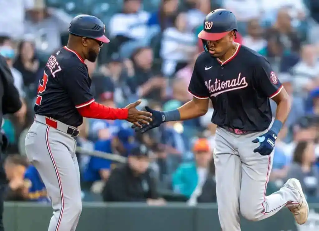 Two baseball players in Nationals uniforms celebrate a successful play, with one high-fiving the other amidst a cheering crowd.