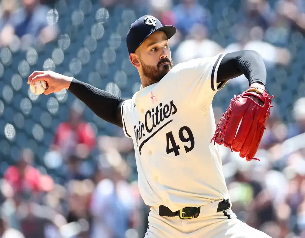 4 Minnesota Twins pitcher winding up for a pitch in a sunlit stadium with the crowd blurred behind him