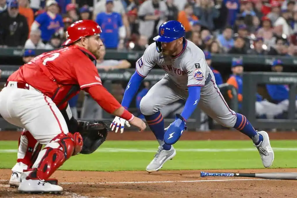 A New York Mets player slides toward home plate as a catcher prepares to make a tag during an intense baseball game.
