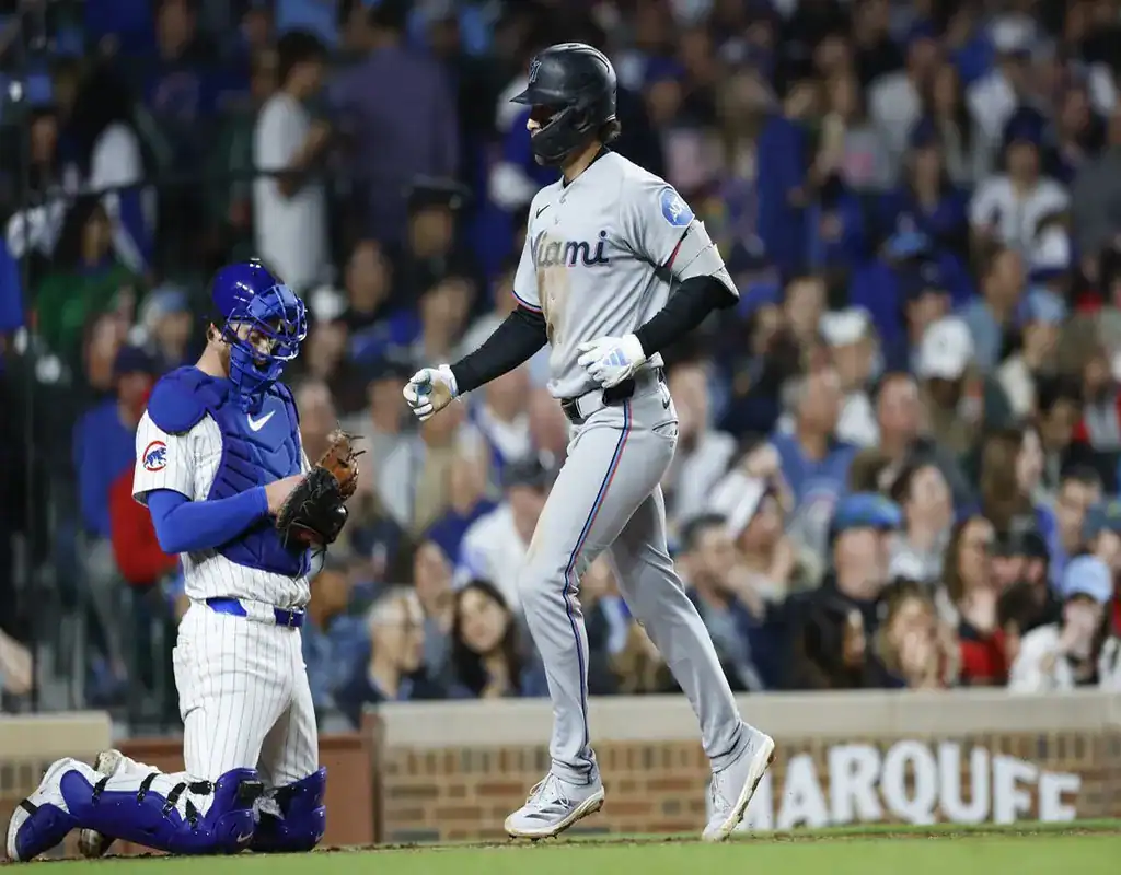 Miami Marlins batter rounding first base as Tampa Bay Rays catcher kneels behind home plate in a packed stadium