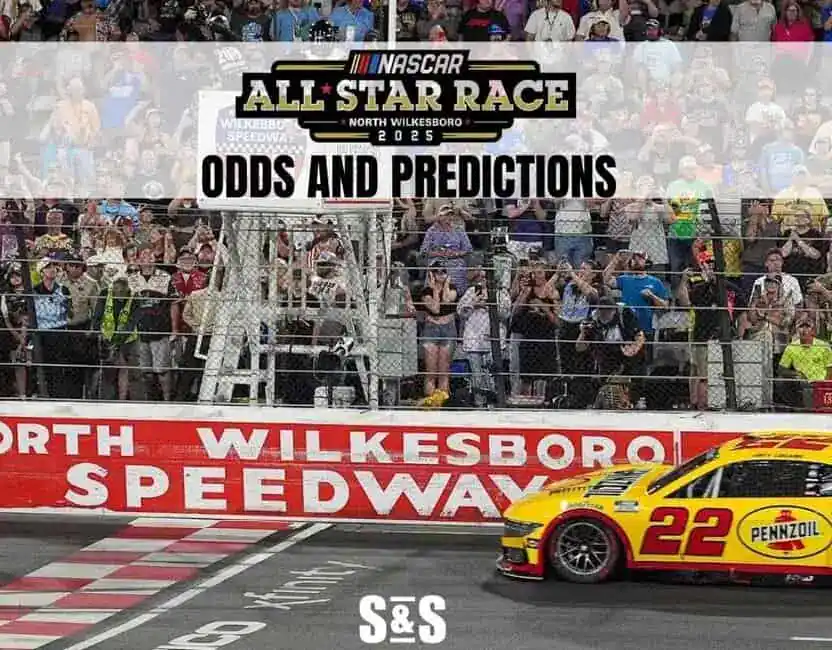 A NASCAR car crosses the finish line at North Wilkesboro Speedway, surrounded by cheering fans and a banner for the 2025 All-Star Race.