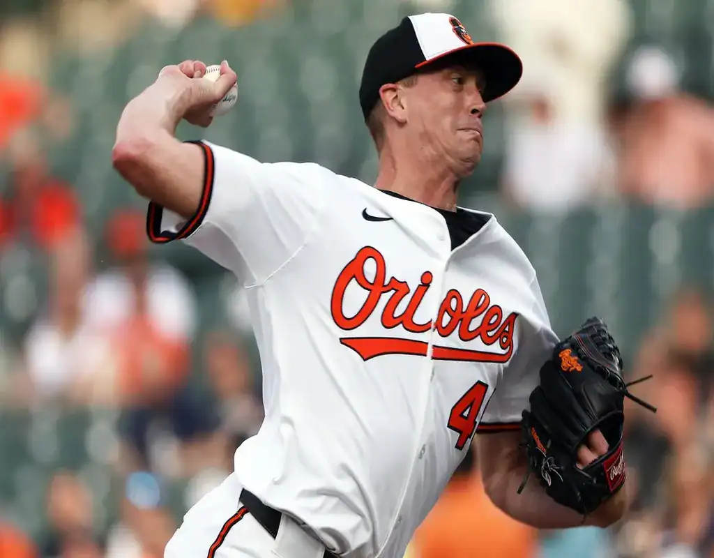 Baltimore Orioles pitcher mid-delivery against a blurred backdrop of fans in the stadium as he throws a pitch