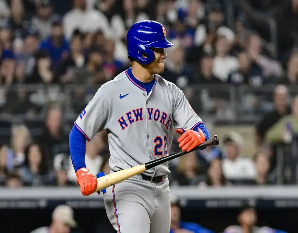 8 New York Mets batter smiling and holding his bat in the on-deck circle with a packed stadium behind him