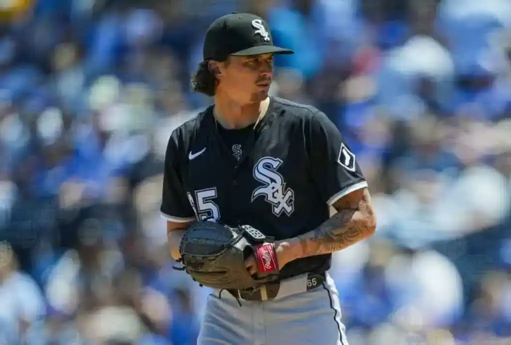 A Chicago White Sox player in a black uniform stands on the pitcher's mound, holding a glove and ball, surrounded by fans in the stands.