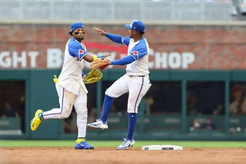 Two baseball players in matching blue and white uniforms celebrate on the field during a game, one is giving a high five.