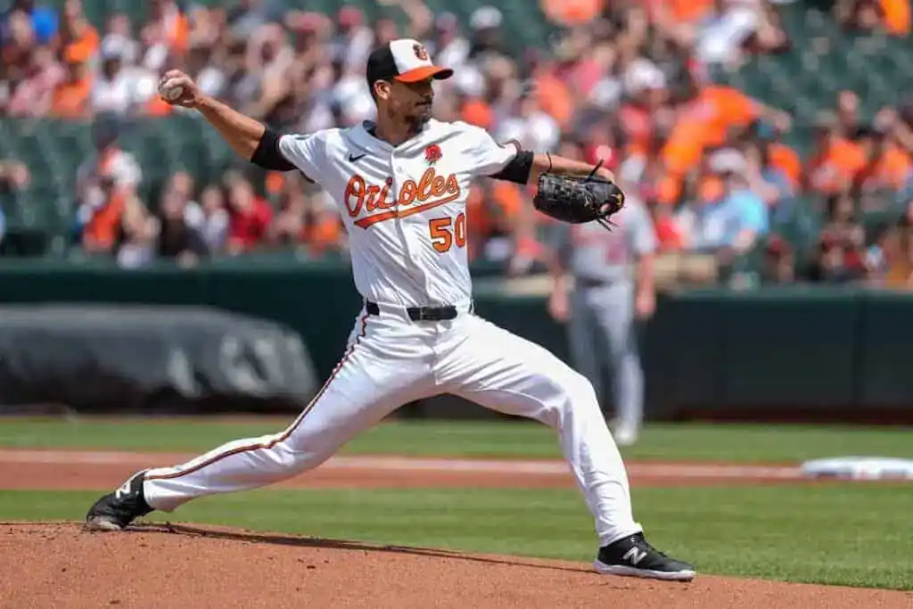 7 A baseball pitcher in an orange and white Orioles uniform winds up to throw a pitch on a sunny day at the stadium, with fans in the background.
