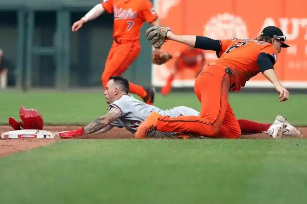 A baseball player slides into second base as an opposing player attempts to tag him out, with teammates in the background.