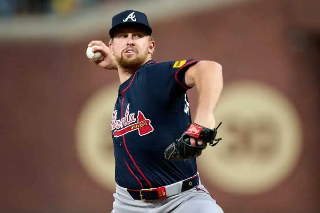 A baseball player in a navy Atlanta Braves jersey winds up to pitch, ready to throw a ball on a baseball field.