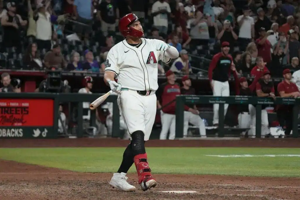 2 A baseball player in a white uniform stands at home plate, bat raised, while fans celebrate in the background during a night game.
