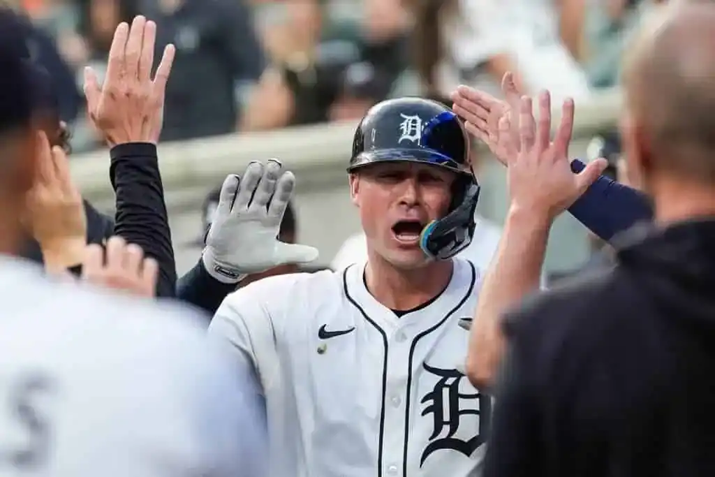 A baseball player in a white jersey celebrating with teammates, exchanging high-fives in a lively stadium atmosphere.