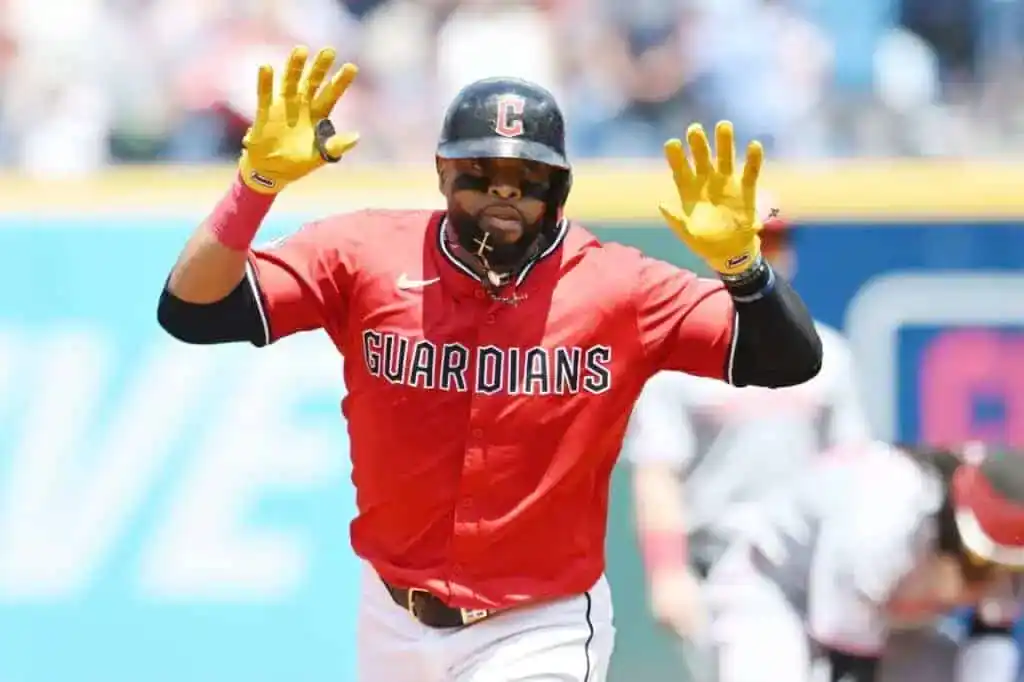 3 A baseball player in a red Guardians jersey celebrates, raising his hands in excitement during a game on a sunny day.