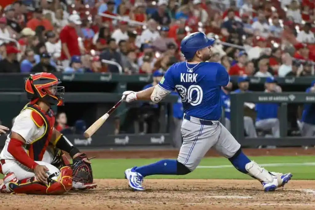 A baseball player in a blue uniform swings a bat, with a catcher in red gear crouching behind him in a packed stadium.