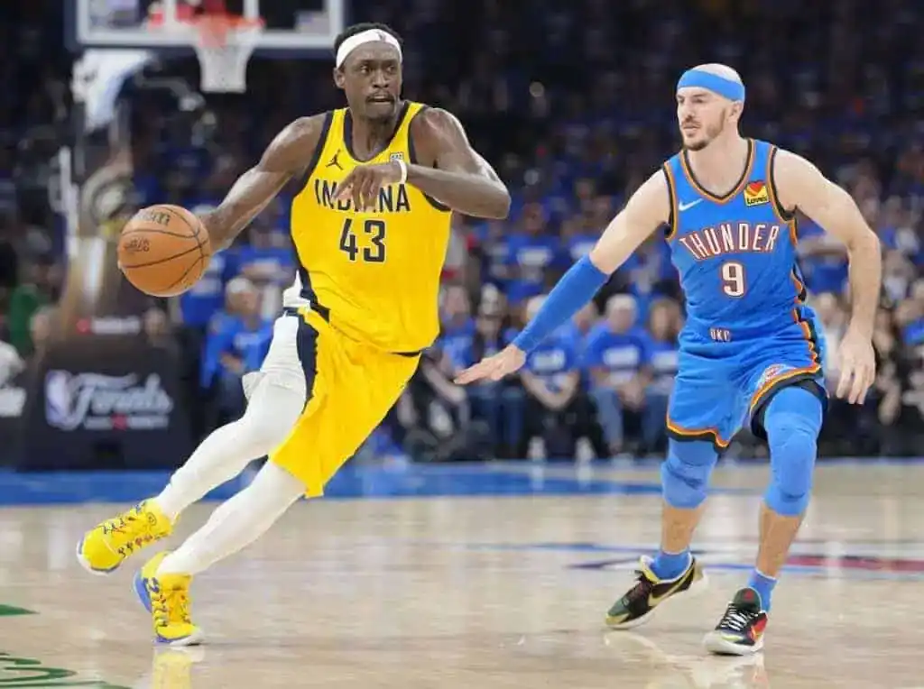A basketball player in a yellow Indiana jersey dribbles past an opponent in a blue Oklahoma City Thunder uniform during a game.